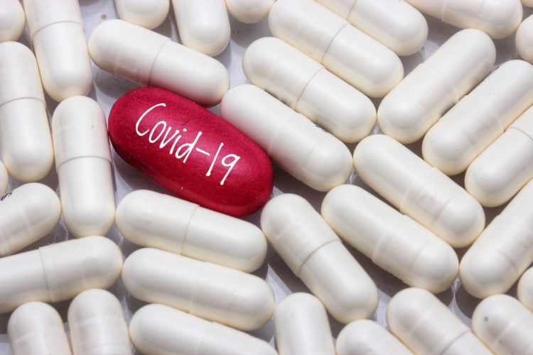 Covid-19 treatment concept - red pill labelled COVID-19 surrounded by blank white capsules