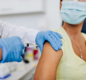 close up of doctor or nurse's gloved hands administering COVID-19 vaccine to a female patient's shoulder.