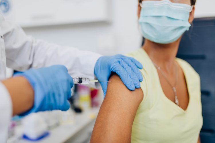 close up of doctor or nurse's gloved hands administering COVID-19 vaccine to a female patient's shoulder.