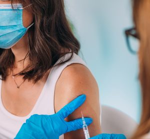 Young Woman wearing a face mask recieving a vaccine in her left arm