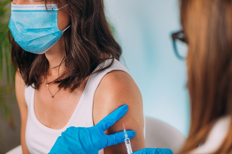 Young Woman wearing a face mask recieving a vaccine in her left arm