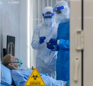 woman on a ventilator in a quarantine room with two doctors in full personal protective equipment taking samples