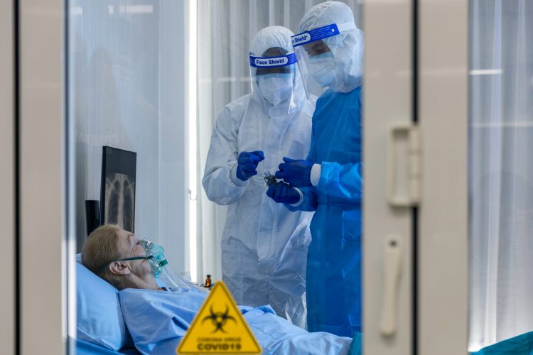 woman on a ventilator in a quarantine room with two doctors in full personal protective equipment taking samples