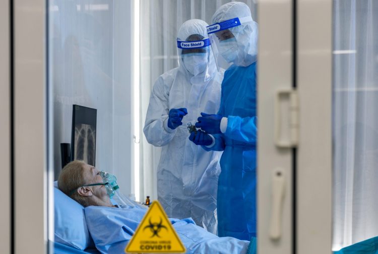 woman on a ventilator in a quarantine room with two doctors in full personal protective equipment taking samples
