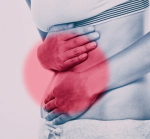 close up of a woman holding her abdomen with red patch over it - idea of inflammatory bowel diseases such as Crohn's disease
