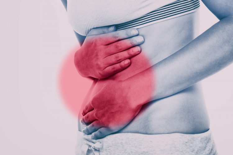 close up of a woman holding her abdomen with red patch over it - idea of inflammatory bowel diseases such as Crohn's disease