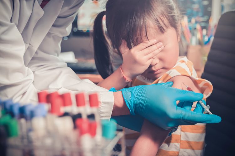 little girl covering her eyes as she is injected by doctor