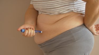 Overweight woman administering an insulin injection with an autoinjector into her stomach
