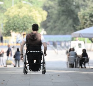 man in a wheelchair pushing himself along a street - may have ALS