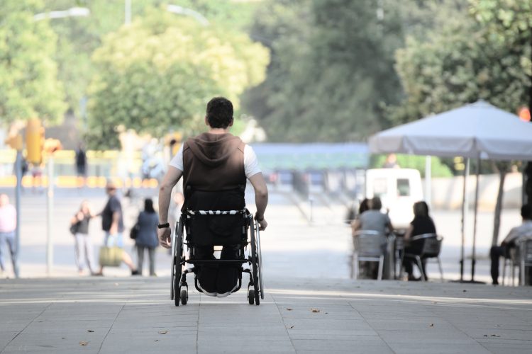 man in a wheelchair pushing himself along a street - may have ALS