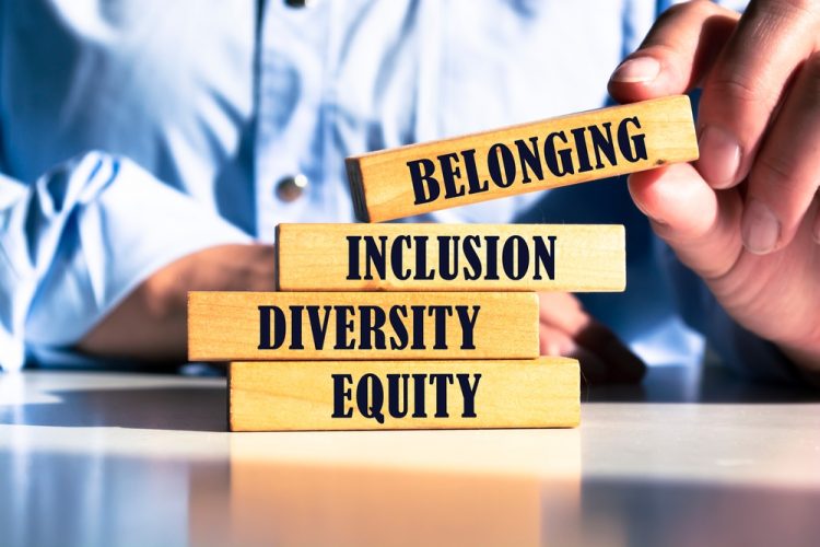 Wooden blocks with words 'equity, diversity, inclusion, belonging' being stacked by a businessman