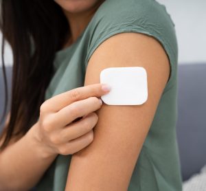 Woman applying a white drug delivery patch to her upper arm