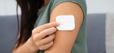 Woman applying a white drug delivery patch to her upper arm