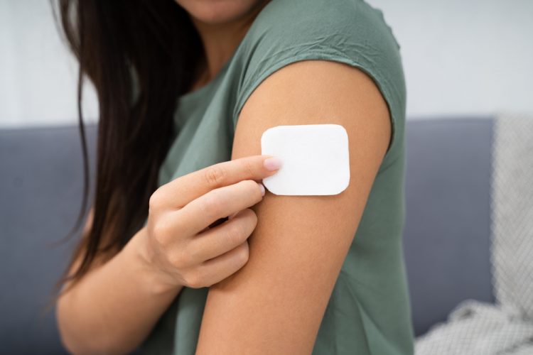 Woman applying a white drug delivery patch to her upper arm