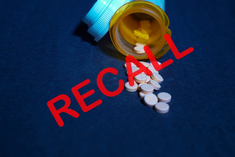 Tablets spilling from a yellow pill bottle with the word recall over the top - idea of a drug recall