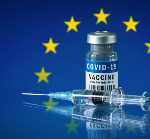 Vial labelled 'COVID-19 VACCINE' with a syringe in front of the EU flag (Blue with a central circle of gold stars)