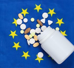 European union flag (Blue with circle of yellow stars in center) with a white pill bottle spilling tablets over it - idea of EU medicine supply