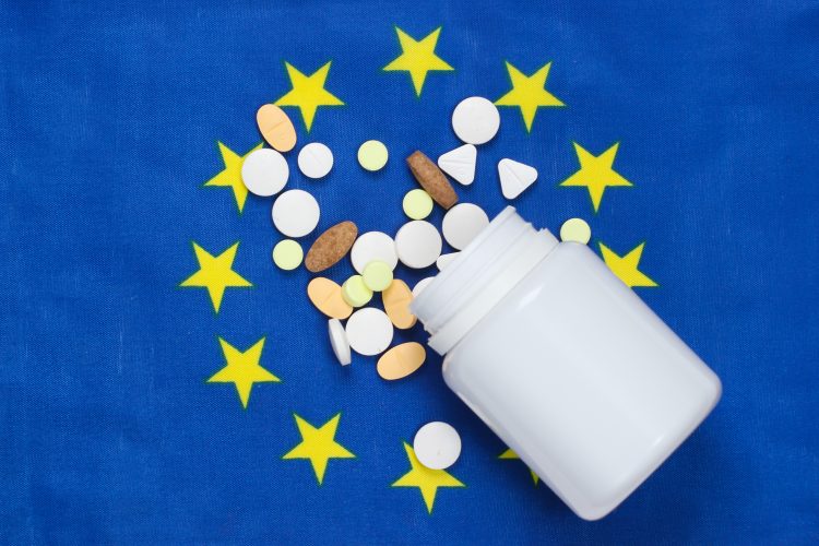 European union flag (Blue with circle of yellow stars in center) with a white pill bottle spilling tablets over it - idea of EU medicine supply