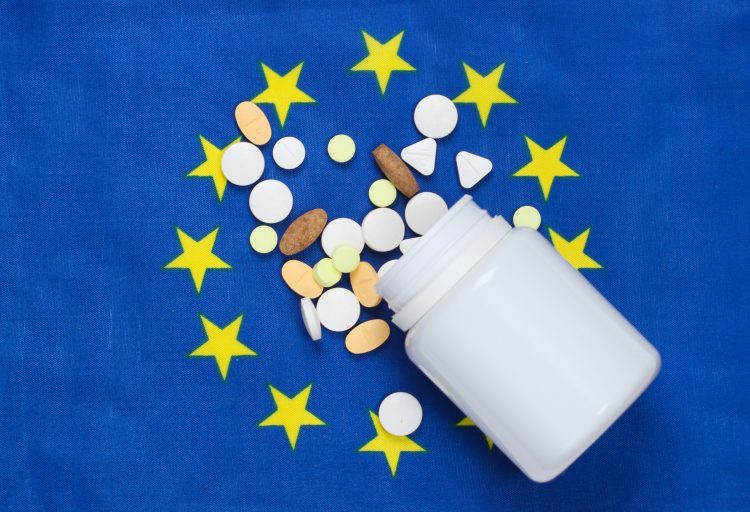 European union flag (Blue with circle of yellow stars in center) with a white pill bottle spilling tablets over it - idea of EU medicine supply