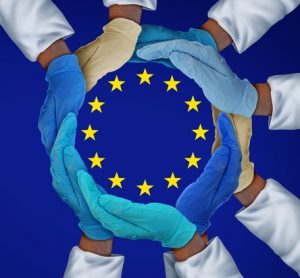 European Union flag (blue with central circle of yellow stars) with glowed hands of people in white coats surrounding the star circle - idea of European medicine/research/drug development/biopharma