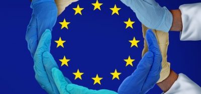 European Union flag (blue with central circle of yellow stars) with glowed hands of people in white coats surrounding the star circle - idea of European medicine/research/drug development/biopharma