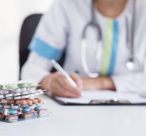 physician writing on a clipboard with blister packages of different tablets next to them