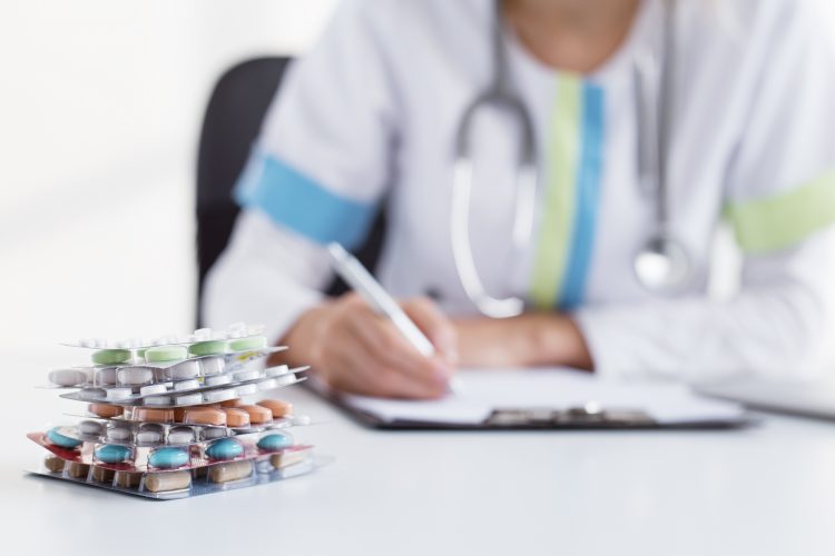 physician writing on a clipboard with blister packages of different tablets next to them