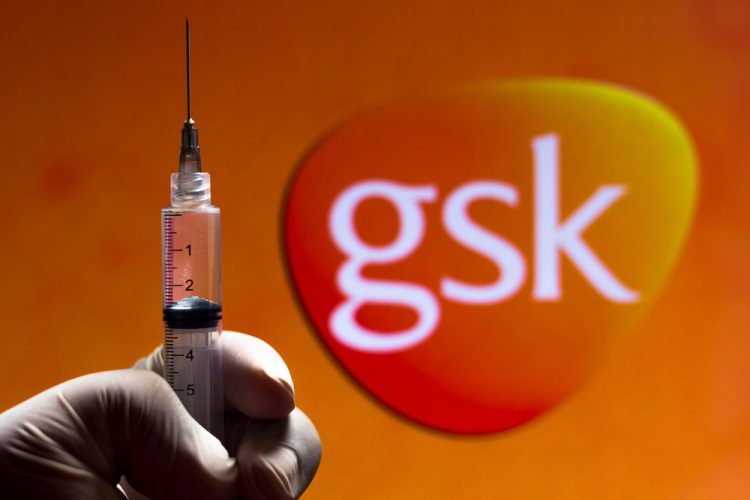 GSK logo (orange rounded corner inverted triangle with GSK lettering in white) with a gloved hand holding a syringe in front - idea of GSK vaccines