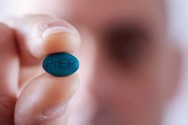 Close up of a person holding up a blue pill etched with 'PrEP' - idea of HIV pre-exposure prophylaxis