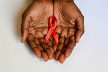 Red HIV ribbon loop held in a Black person's cupped hands
