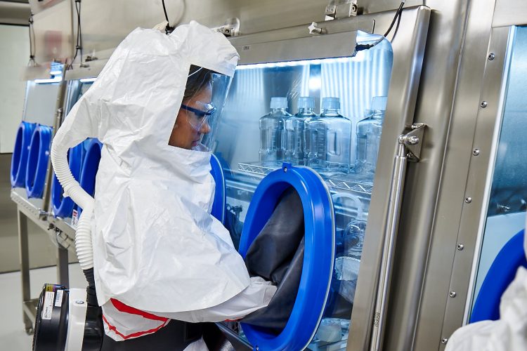 woman in white hazard suit and respiratory gear with hands in a vacuum chamber