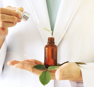 Idea of herbal/plant-based medicine: scientist holding a dropper and amber vial