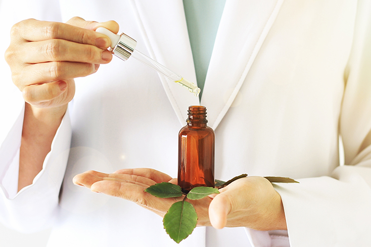 Idea of herbal/plant-based medicine: scientist holding a dropper and amber vial