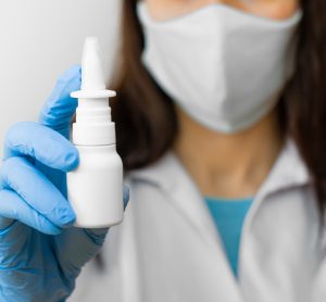 Female doctor wearing personal protective equipment holding out a nasal spray