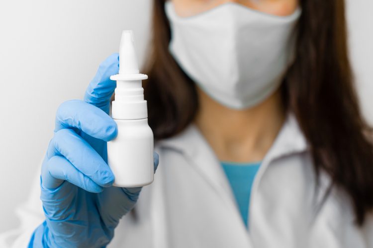 Female doctor wearing personal protective equipment holding out a nasal spray