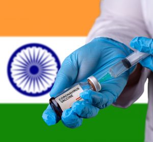 Doctor drawing liquid into a syring from a vial labelled 'COVID-19 VACCINE', in front of an Indian flag (Horizontal stripes orange, white and green) - idea of COVID-19 vaccines being developed/authorised in India