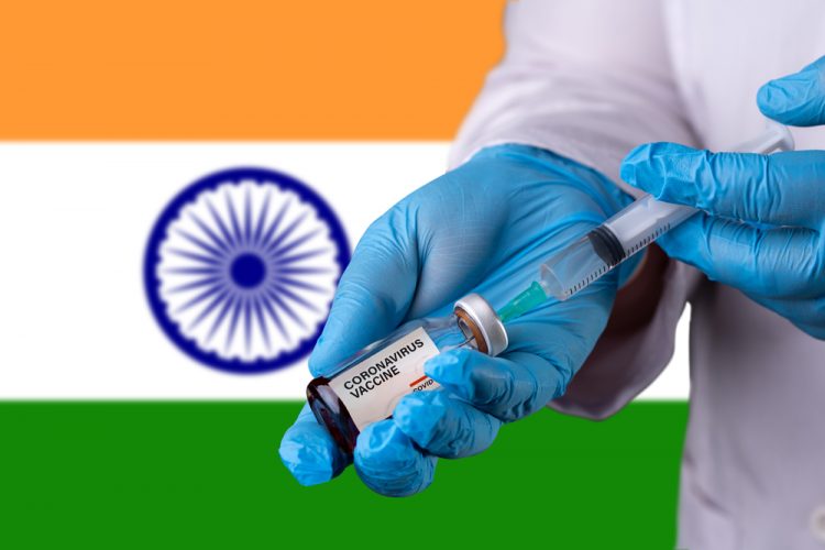 Doctor drawing liquid into a syring from a vial labelled 'COVID-19 VACCINE', in front of an Indian flag (Horizontal stripes orange, white and green) - idea of COVID-19 vaccines being developed/authorised in India