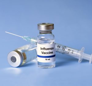 Vial labelled 'influenza vaccine' next to a syringe on a blue background