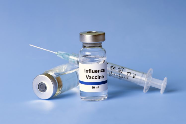 Vial labelled 'influenza vaccine' next to a syringe on a blue background