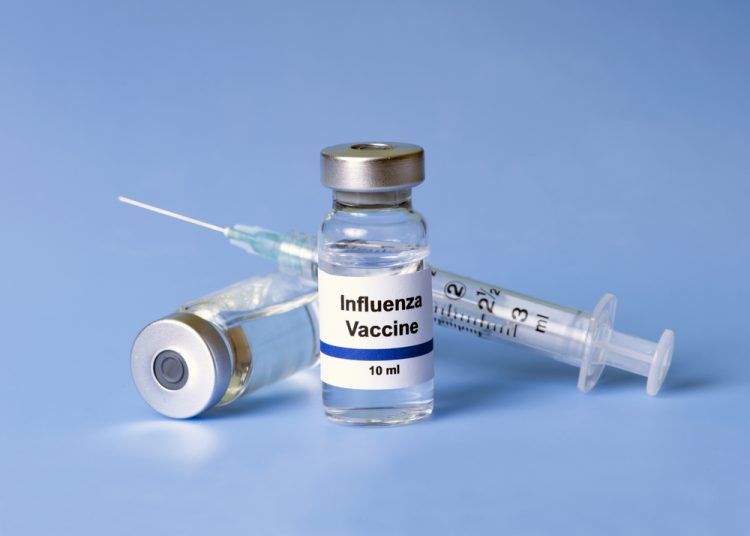 Vial labelled 'influenza vaccine' next to a syringe on a blue background