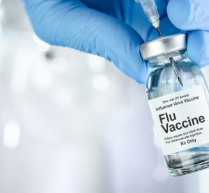 hand in blue medical gloves holding vial labelled 'Influenza, Flu Vaccine'