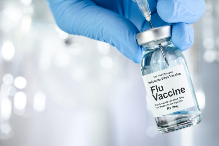 hand in blue medical gloves holding vial labelled 'Influenza, Flu Vaccine'