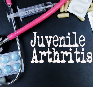 Words 'Juvenile Arthritis' surrounded by medicines and a stethoscope - idea of treatments for juvenile arthritis