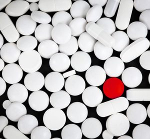 One red pill surrounded by various shapes of white pills - idea of counterfeit pharmaceuticals