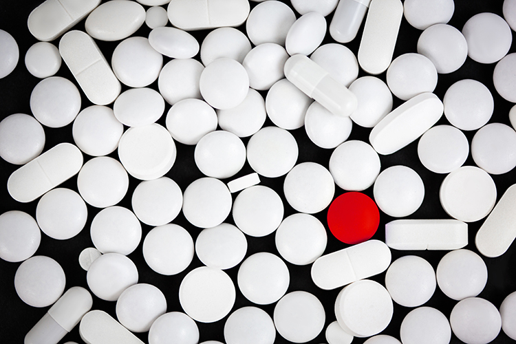 One red pill surrounded by various shapes of white pills - idea of counterfeit pharmaceuticals