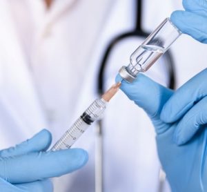 Doctor, nurse or scientist hand in blue nitrile gloves drawing a clear liquid into a syringe from a vial - idea of a vaccine or injection