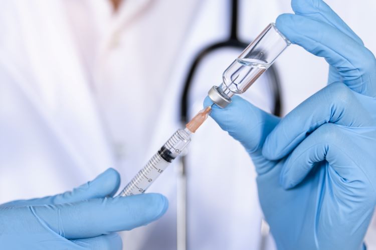 Doctor, nurse or scientist hand in blue nitrile gloves drawing a clear liquid into a syringe from a vial - idea of a vaccine or injection