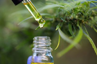 pipette dropping yellow coloured oil into a glass bottle superimposed over a cannabis flower