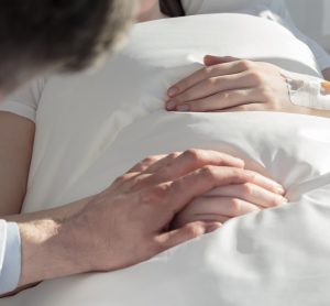 Man in white coat (oncologist) holding hand of female cancer patient in a hospital bed