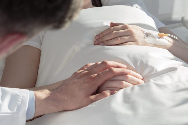 Man in white coat (oncologist) holding hand of female cancer patient in a hospital bed